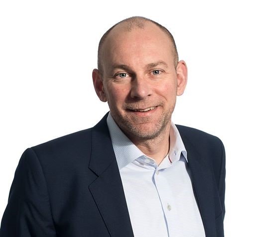 Bald man in a navy suit and white shirt smiling against a plain white background.