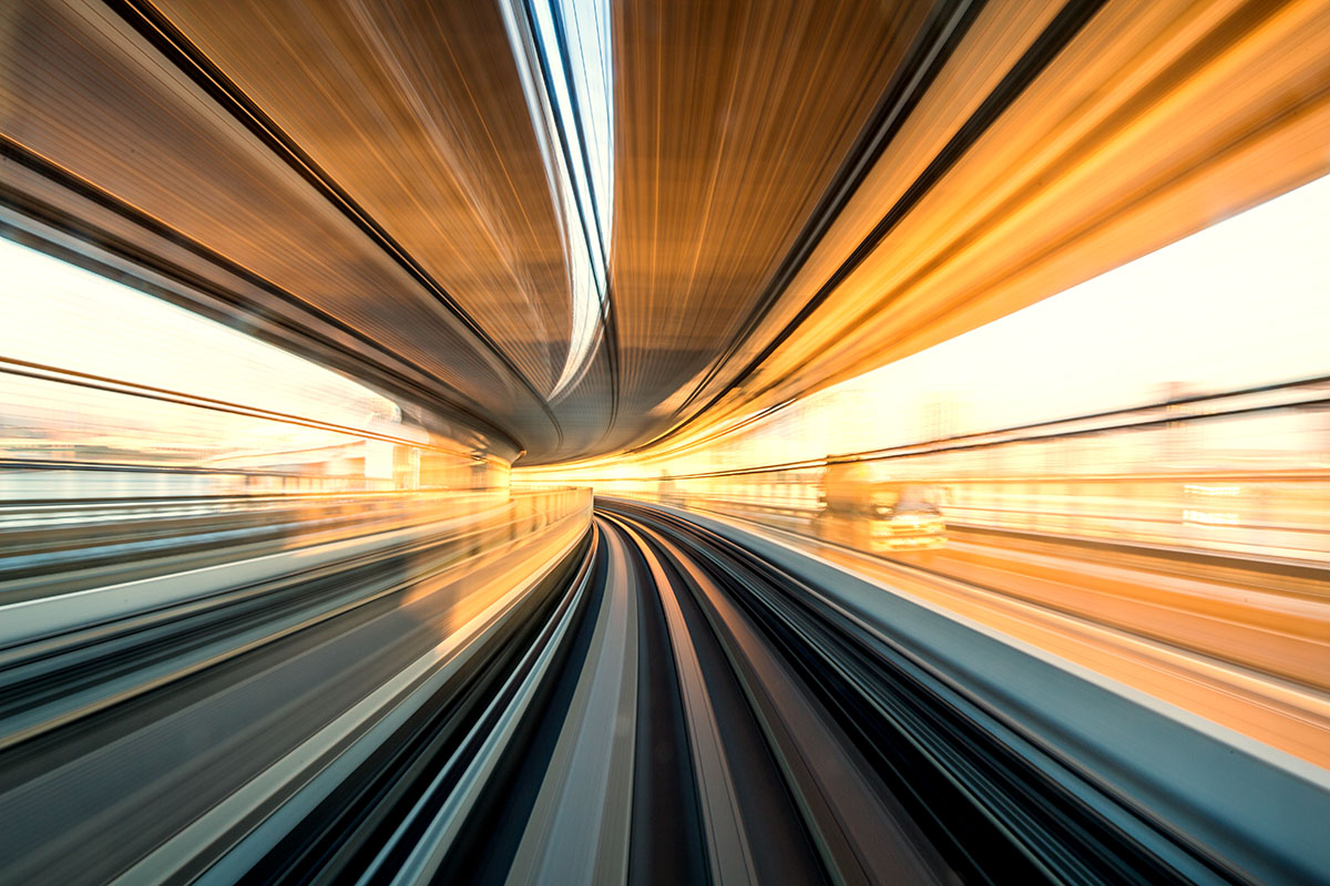 Blurred view from front of a moving train on curving tracks, yellow lights streaking for a sense of high speed.