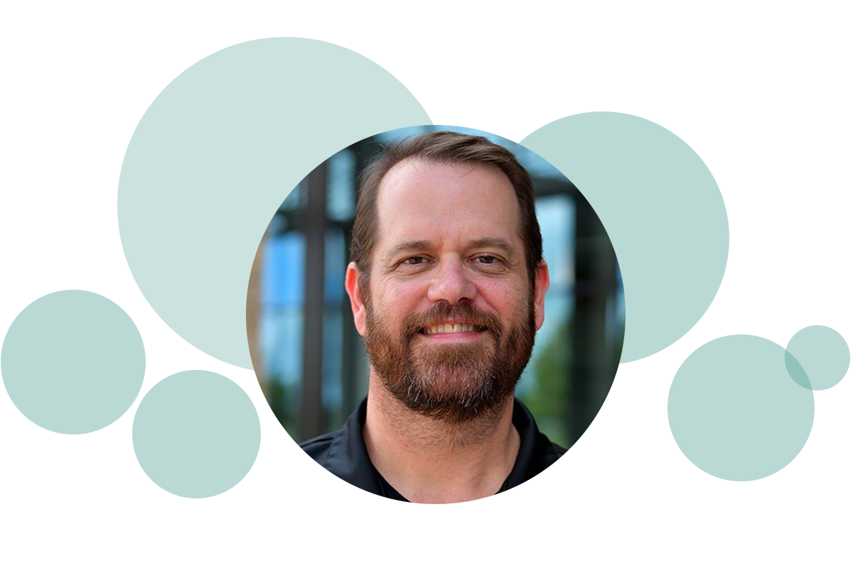Smiling bearded man in a circular frame with overlapping teal circles in the background.